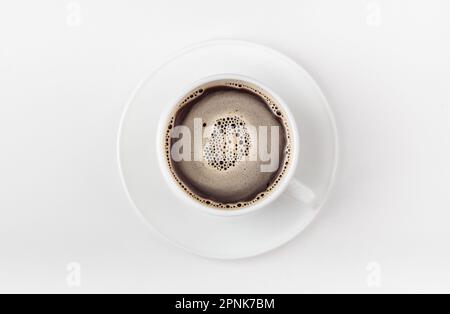 Eine weiße Tasse Kaffee auf weißem Hintergrund. Morgenkaffee mit Kaffeeschaum. Draufsicht. Stockfoto