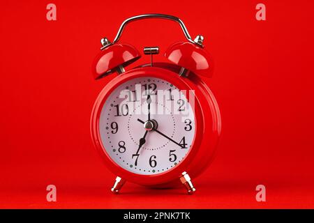 Roter Wecker auf rotem Hintergrund. Es ist 7 Uhr. Guten Morgen. Stockfoto