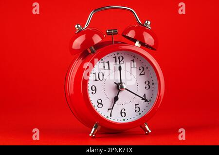 Roter Wecker auf rotem Hintergrund. Es ist 7 Uhr. Guten Morgen. Stockfoto