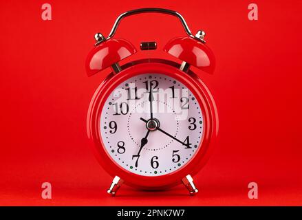 Roter Wecker auf rotem Hintergrund. Es ist 7 Uhr. Guten Morgen. Stockfoto