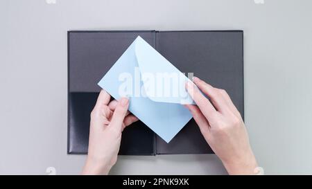 Blauer Mockup-Umschlag mit leerem Platz für Text und Design in der Hand einer jungen Frau auf grauem Hintergrund. Brett, leer, Vorlage, Modell, Geschenk, Buch, Greeti Stockfoto