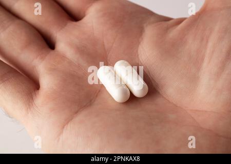 Männliche Hand, die zwei Pillen in der Hand hält, auf grauem Hintergrund, und Ihre Medikamente nimmt. Schließen Stockfoto