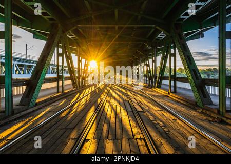 Warschau, Polen - 2022. Juli: Lange Gdanski-Brücke aus Holz und Metall mit Straßenbahnschienen und grünem Dach am Morgen zur goldenen Stunde bei Sonnenaufgang Stockfoto