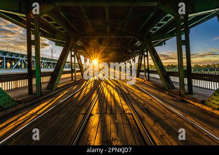 Warschau, Polen - 2022. Juli: Lange Gdanski-Brücke aus Holz und Metall mit Straßenbahnschienen und grünem Dach am Morgen zur goldenen Stunde bei Sonnenaufgang Stockfoto