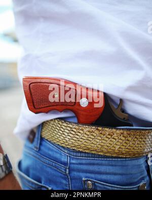 Ein Mann versteckt eine Waffe hinter einem Hosengürtel. Stockfoto