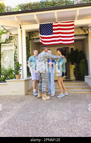 Fröhliche, vielfältige Freunde mit usa-Flaggen, begrüßen birassistische männliche amerikanische Soldaten Stockfoto