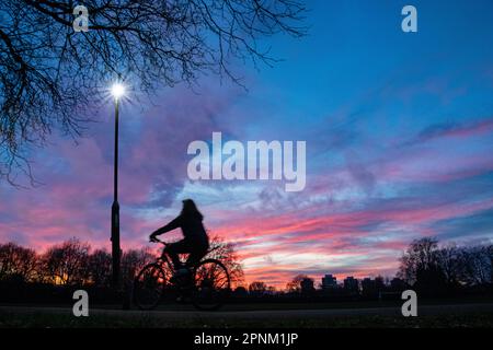 Ein Radfahrer fährt durch einen Londoner Park bei Sonnenuntergang unter Ampel Stockfoto