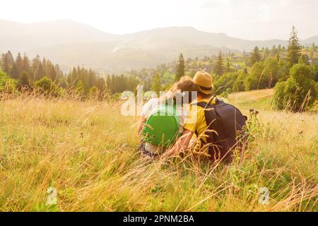Rückansicht. Glückliches junges Paar, das auf den Bergen sitzt, ein Paar, das die Aussicht auf die Berge sieht, lieben Natururlaub Grüne Reise lieben Urlaub Sommer Stockfoto