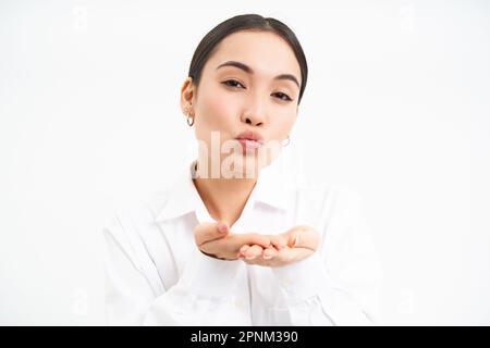 Nahaufnahme des Porträts einer süßen Bürofrau, die einen Luftkuss auf die Handflächen sendet, die Lippen kotzt und vor der Kamera weich wirkt, steht auf weißem Hintergrund Stockfoto