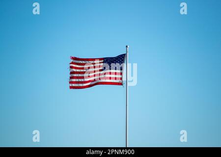 Ein ruhiger, wolkenloser Himmel in Rot, Weiß und Blau bietet eine patriotische Kulisse für eine amerikanische Flagge, die im Wind auf dem Pol weht. Stockfoto