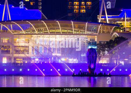 Große Menschenmassen versammeln sich auf der Uferpromenade der Marina Bay Shoppes in Singapur, um die abendliche „Spectra Light and Water Show“ zu sehen. Stockfoto