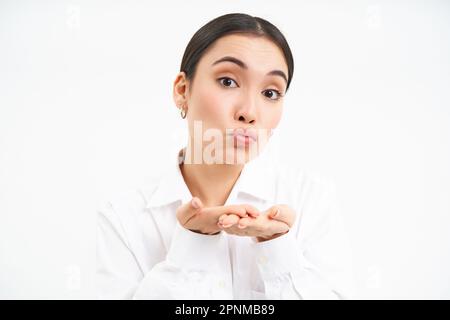 Nahaufnahme des Porträts einer süßen Bürofrau, die einen Luftkuss auf die Handflächen sendet, die Lippen kotzt und vor der Kamera weich wirkt, steht auf weißem Hintergrund Stockfoto