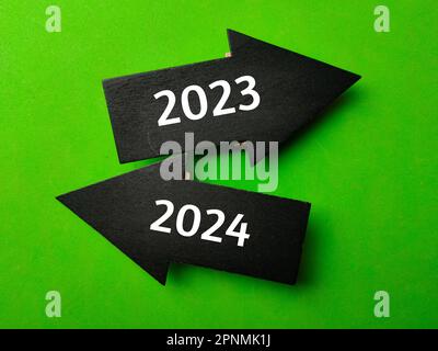 Schwarzer Holzpfeil mit den Ziffern 2023 und 2024 auf grünem Hintergrund Stockfoto