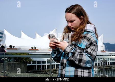 Teenager Touristenmädchen geht, während es notwendig ist Spielen Sie mit Vancouver im Stadtzentrum an der Waterfront Station Mädchen vor dem Hintergrund von weißen Segeln schaut auf das Telefon und sucht nach geolokalisierter Route Stockfoto