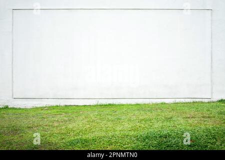 Große weiße Wand mit quadratischem Rahmen und grünem Gras im Vordergrund. Frontalansicht einer hellen Hausfassade als Hintergrund Stockfoto