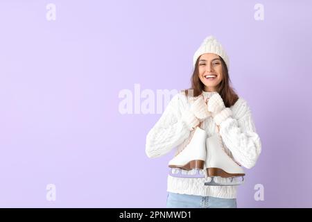 Hübsche junge Frau mit Schlittschuhen auf lila Hintergrund Stockfoto