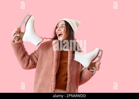 Hübsche junge Frau mit Schlittschuhen auf pinkfarbenem Hintergrund Stockfoto