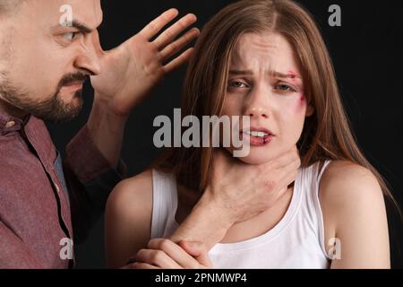 Ein wütender junger Mann, der seine Frau an der Kehle hält, auf dunklem Hintergrund, Nahaufnahme. Das Konzept der häuslichen Gewalt Stockfoto