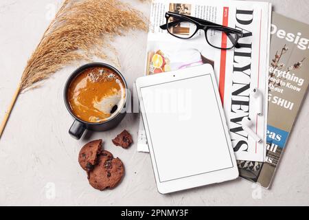 Tasse Kaffee mit Keks, Tablet-Computer und Zeitung auf weißem Hintergrund Stockfoto