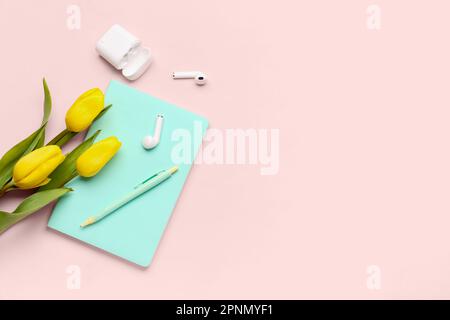 Moderne Kopfhörer, Notizbuch, Stift und wunderschöne Tulpenblumen auf pinkfarbenem Hintergrund Stockfoto