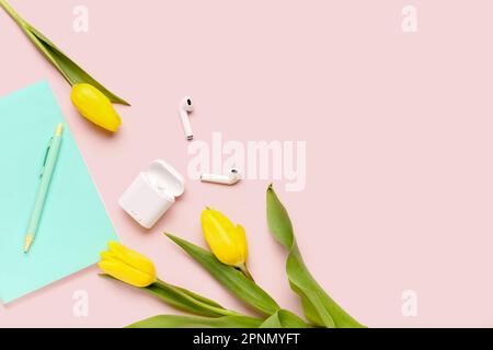 Moderne Kopfhörer, Notizbuch, Stift und wunderschöne Tulpenblumen auf pinkfarbenem Hintergrund Stockfoto