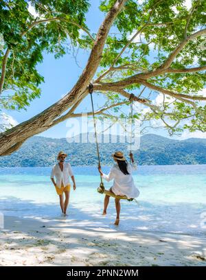 Ein paar Männer und Frauen sind am Strand mit einer Seilschaukel auf Koh Lipe Island Süd Thailand mit türkisfarbenem Meer und weißem Sandstrand bei Ko Lipe. Tarutao-Nationalpark, Insel Koh Rawi Stockfoto