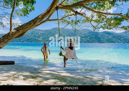 Ein paar Männer und Frauen sind am Strand mit einer Seilschaukel auf Koh Lipe Island Süd Thailand mit türkisfarbenem Meer und weißem Sandstrand bei Ko Lipe. Tarutao-Nationalpark, Insel Koh Rawi Stockfoto