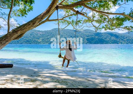 Eine Frau, die unter einem Baum schwingt, an einer Schaukel am Strand von Koh Lipe Island Süd-Thailand mit türkisfarbenem Meer und weißem Sandstrand bei Ko Lipe. Tarutao-Nationalpark, Insel Koh Rawi Stockfoto