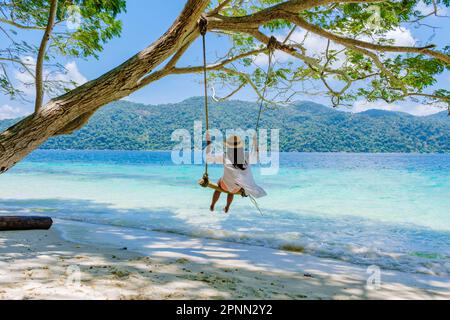 Eine Frau, die unter einem Baum schwingt, an einer Schaukel am Strand von Koh Lipe Island Süd-Thailand mit türkisfarbenem Meer und weißem Sandstrand bei Ko Lipe. Tarutao-Nationalpark, Insel Koh Rawi Stockfoto