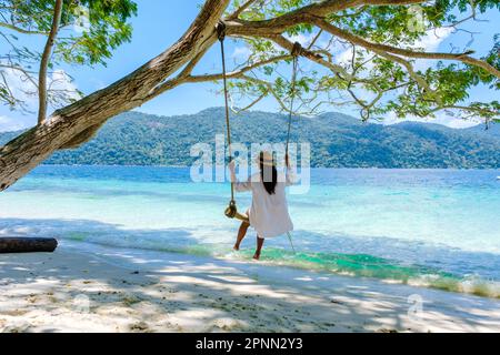 Eine Frau, die unter einem Baum schwingt, an einer Schaukel am Strand von Koh Lipe Island Süd-Thailand mit türkisfarbenem Meer und weißem Sandstrand bei Ko Lipe. Tarutao-Nationalpark, Insel Koh Rawi Stockfoto
