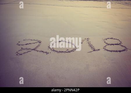 Zahlen 2018 handgeschrieben auf Sand am Strand im Hintergrund bei Sonnenuntergang Stockfoto