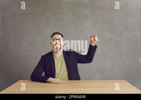 Ein glücklicher lächelnder Mann sitzt am Schreibtisch und hält ein unsichtbares Studiofoto Stockfoto