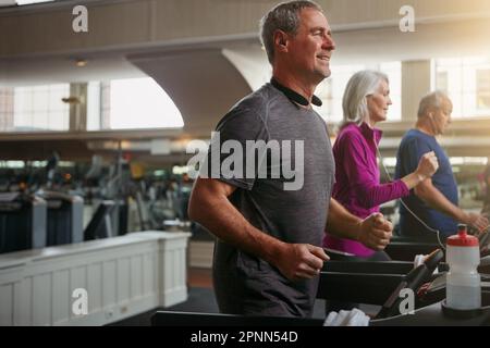 Entschlossen, fit zu werden und fit zu bleiben. Eine Gruppe erwachsener Menschen, die auf Laufbändern im Fitnessstudio trainieren. Stockfoto