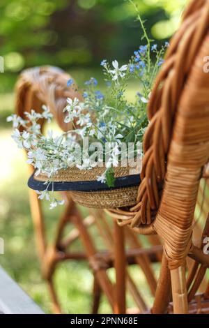 Langsames Leben. Strohhut auf einem Korbstuhl im Garten. Romantische Sommerszene Stockfoto