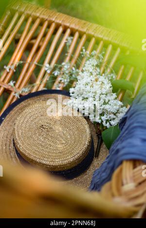 Langsames Leben. Ein Strohhut mit Blumen liegt auf einem Korbstuhl. Blick von oben. Stockfoto