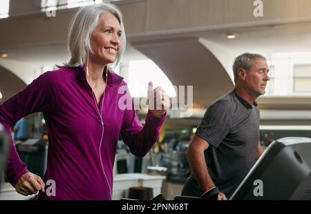 Fokussiert und entschlossen, seine Fitnessziele zu erreichen. Eine reife Frau und ein Mann, die im Fitnessstudio auf Laufbändern trainieren. Stockfoto