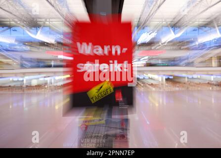 20. April 2023, Hamburg: Ein Poster aus Verdi mit dem Text „Warning Strike today“ hängt auf einer Anzeigetafel in Terminal 1 am Flughafen Hamburg. Die Gewerkschaft Verdi hat auf drei Flughäfen, darunter Hamburg, einen Warnstreik gefordert. Hintergrund für die Warnschläge sind die Verhandlungen zwischen Verdi und dem Bundesverband der Flugsicherheitsgesellschaften (BDLS) über Zeitzuschläge für Nacht-, Samstag-, Sonntag- und Urlaubsarbeit sowie eine bessere Tarifvereinbarung über die Überstundenvergütung für Sicherheits- und Servicepersonal auf kommerziellen Flughäfen. Foto: Christian Charisius/dpa Stockfoto