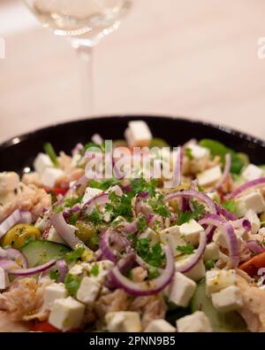 Ein köstlicher Salat und ein Glas Weißwein auf einem weißen Tisch, bereit zum Genießen Stockfoto