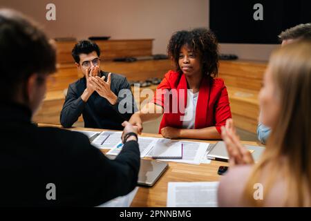 Rückansicht eines kaukasischen Geschäftsmanns, der nach Vertragsunterzeichnung mit einer afrikanischen Geschäftsfrau Hand schüttelt, Mitglieder, die klatschende Hände trafen Stockfoto