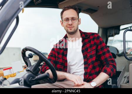 Junger Fahrer eines Traktors oder Mähdreschers für den ländlichen Raum, der in der Kabine sitzt. Landwirtschaft und Ernte. Landwirtschaft und Ernte Stockfoto