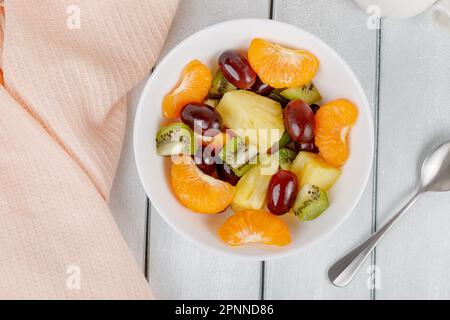 Obstsalat mit Ananas, Orange, Kiwi und Trauben auf einem Teller mit Holzhintergrund. Hochwertiges Foto Stockfoto