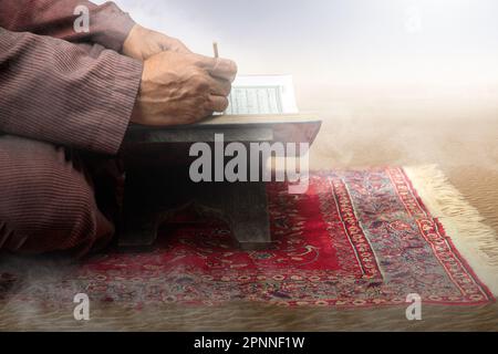 Muslimischer Mann, der in der Wüste auf dem Gebetsvorleger sitzt und den Koran liest Stockfoto