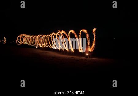 Rotierender Kreis feuriger Flammen, der sich auf den Mann zubewegt, der im Dunkeln hockt. Stockfoto