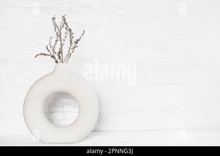 Getrocknete Blumen in stilvoller Keramikvase auf einem Tisch. Zeitgenössisches, gemütliches Interieur. Leerzeichen für Text. Holzmauer Im Nordischen Hintergrund. Minimalistisch Stockfoto