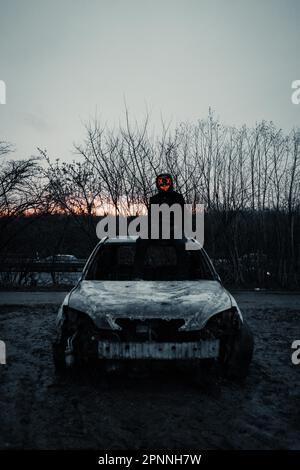 Purge-Maske, Mann mit LED-Maske auf einem ausgebrannten Auto, Frankfurt am Main, Hessen, Deutschland Stockfoto