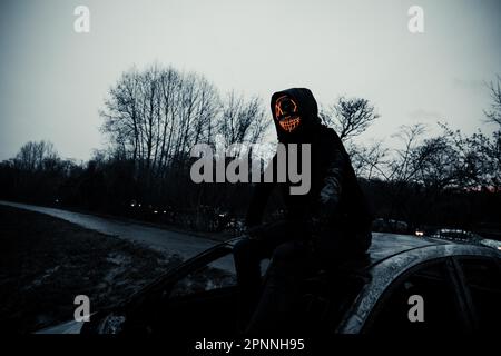 Purge-Maske, Mann mit LED-Maske auf einem ausgebrannten Auto, Frankfurt am Main, Hessen, Deutschland Stockfoto