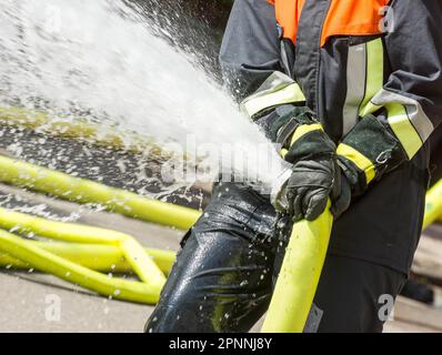 Wasser, das aus einem Feuerwehrschlauch spritzt, der von einem Feuerwehrmann gehalten wird Stockfoto