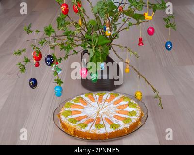 Hausgemachter Karottenkuchen vor einem Strauch mit Osterdekorationen Stockfoto