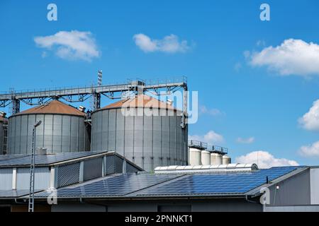 Nahaufnahme von Silbersilos in einer landwirtschaftlichen Verarbeitungsanlage zur Verarbeitung, Trocknung, Reinigung und Lagerung landwirtschaftlicher Erzeugnisse und Solarpaneele. Stockfoto