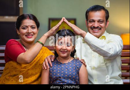 Glückliches indisches Paar, das sich wie eine Hausgeste an Mädchen hält, indem es in die Kamera schaut - Konzept von Elternschutz, Empowerment und Kinderbetreuung Stockfoto